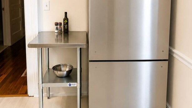 Un frigorífic d'acer inoxidable al costat d'una taula metàl·lica petita amb un bol i condiments.