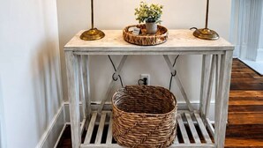 A white console table with two lamps, a framed map, and a basket underneath.