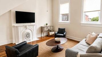 A modern living room with a fireplace, a television, a ceiling fan, and a large window.