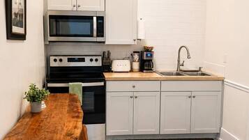 A compact kitchen with white cabinetry, a microwave, a stove, a sink, and a wooden table with two chairs.