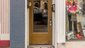 Fachada com porta de madeira com a placa '116', vitrine com manequins e parede de tijolos.