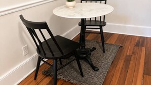 A small dining area with a round table, two chairs, a potted plant, and a rug on wooden flooring.