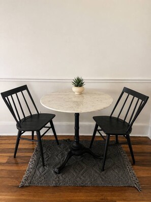A round table with a single plant, flanked by two chairs, on a textured rug.