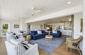 A spacious living area with striped sofas, a blue sectional, and a kitchen in the background. - Stunning Oceanfront Home, Guest Cards & Golf Cart (Fripp Island)