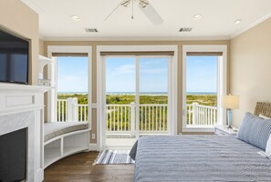 Une chambre dotée d’un grand lit, d’une télévision, d’une cheminée et d’un balcon offrant une vue sur la plage.