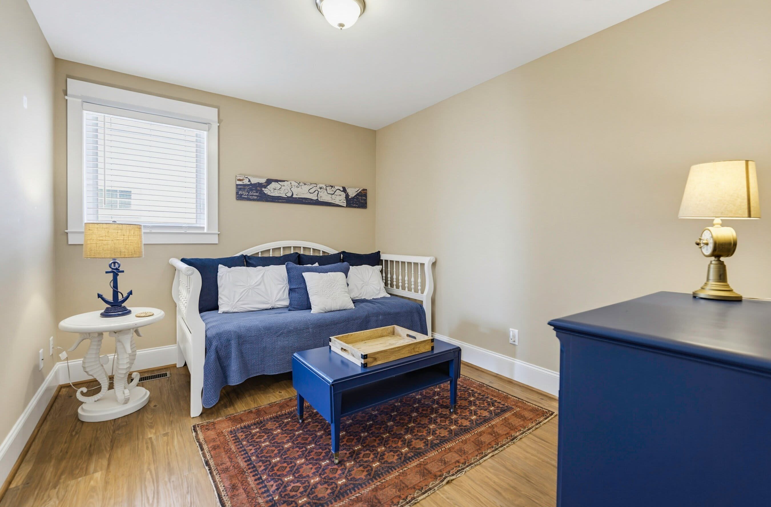A bedroom with a bed, a small table, a lamp, a rug, and a wall art piece.