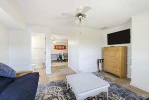 A room with a bed, a television, a ceiling fan, a wooden dresser, and a bathroom visible through an open door. - Stunning Oceanfront Home, Guest Cards & Golf Cart (Fripp Island)