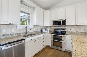 A modern kitchen with white cabinetry, stainless steel appliances, and a granite countertop. - Stunning Oceanfront Home, Guest Cards & Golf Cart (Fripp Island)