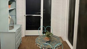 Een kamer met een witte bakstenen muur, een witte deur, een kroonluchter, een tafel met stoelen en een blauwe kast.