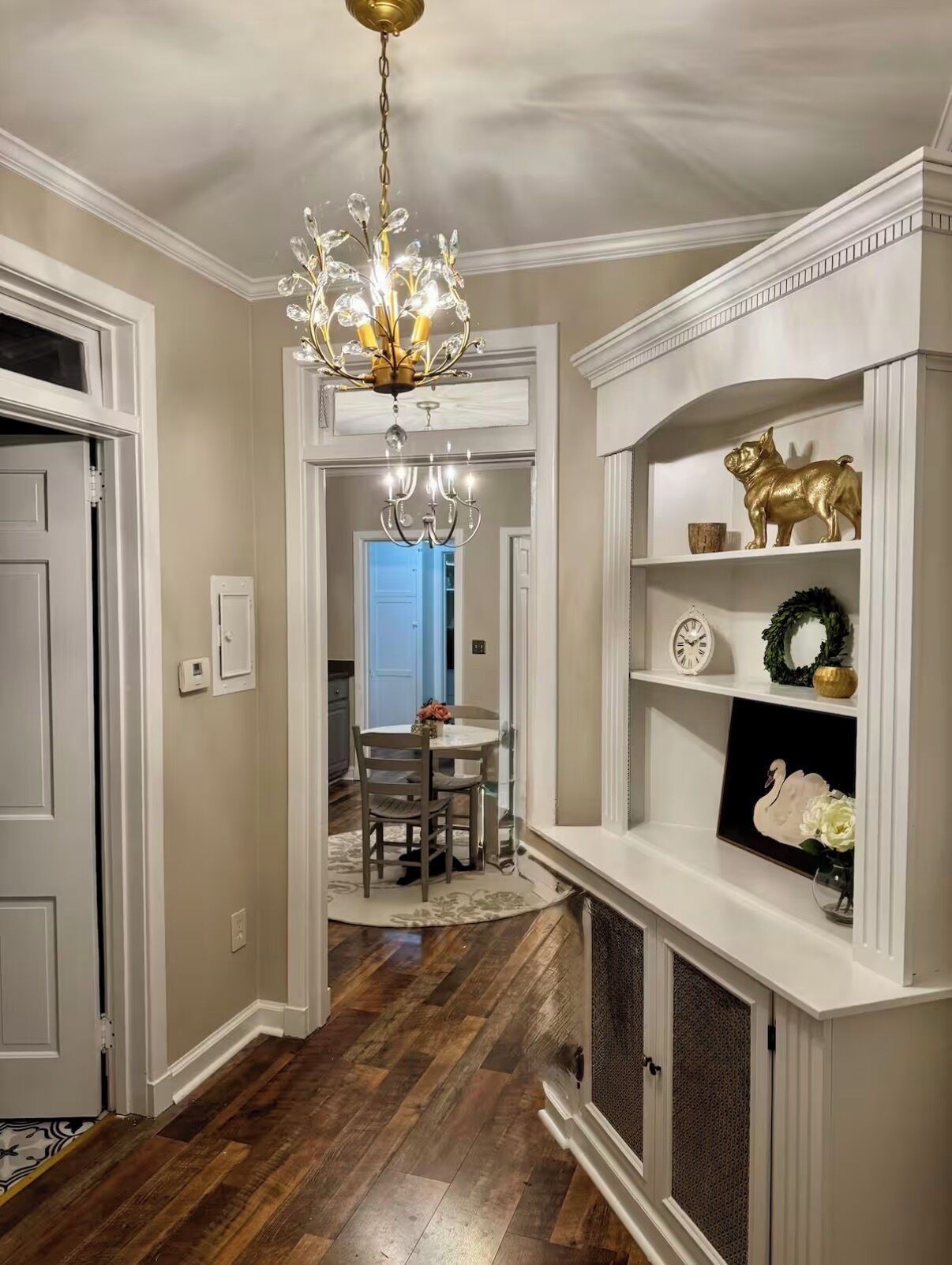 Un couloir agrémenté d’un lustre, un coin repas avec une table et des chaises, et une étagère ornée d’objets décoratifs.