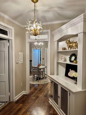 Un corridoio con un lampadario, una sala da pranzo con tavolo e sedie, e una mensola con oggetti decorativi.
