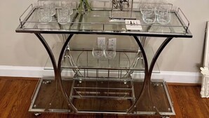 Een glazen tafel met metalen poten, een vaas met bloemen en een ingelijst beeld op de muur.