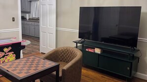 Een woonkamer met een houten vloer, een televisie op een meubel, een stoel en een tafel met een schaakbord.