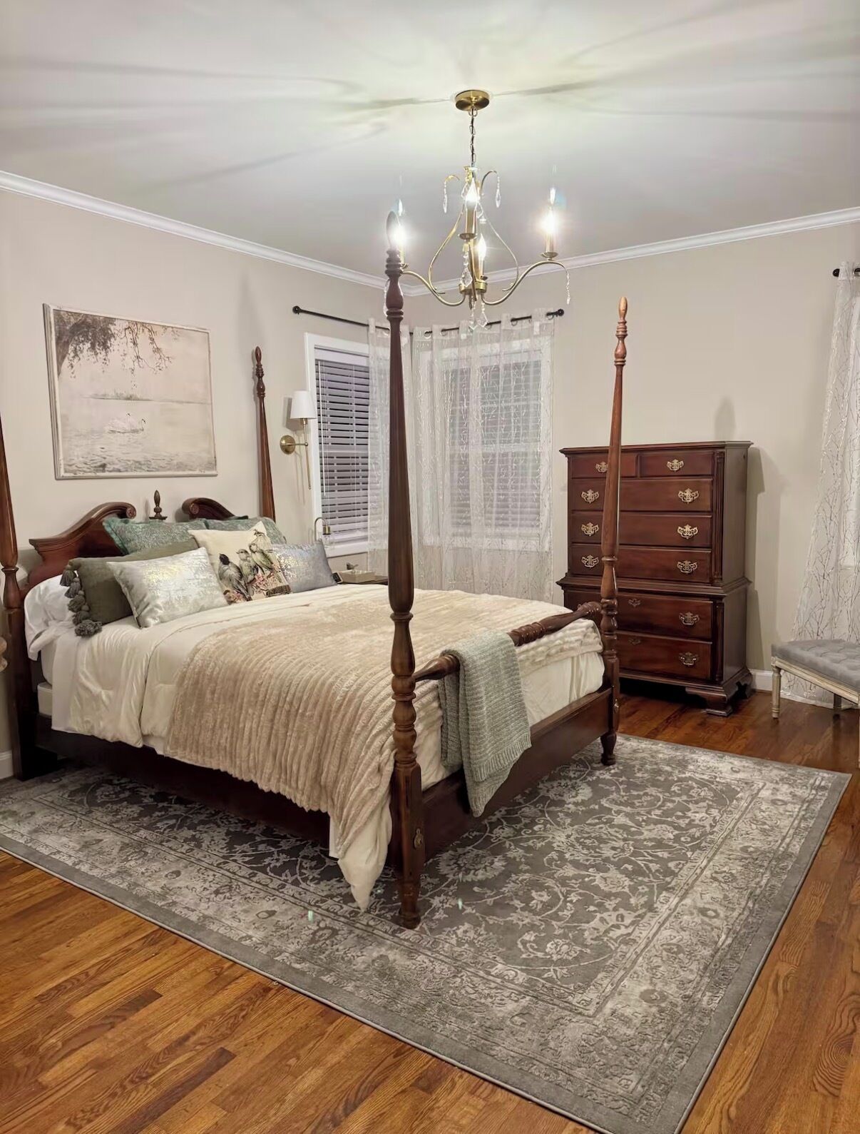 Une chambre à coucher avec un lit à baldaquin, une commode, un lustre et une grande fenêtre avec des stores.
