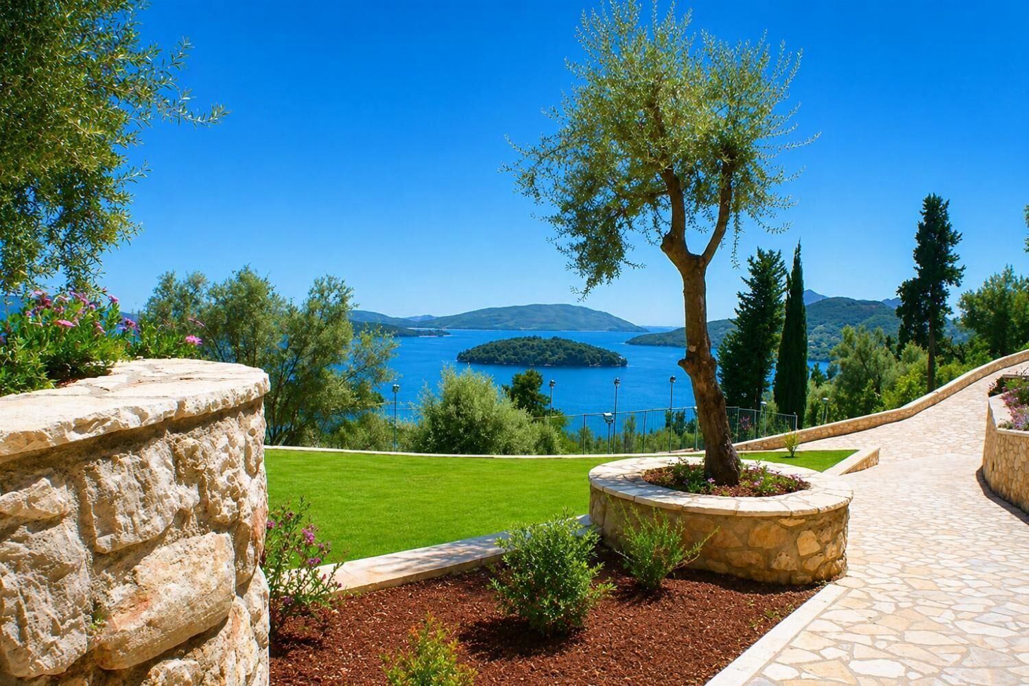 Ein angelegter Garten mit einer Steinsäule, einem Baumbeet und Blick auf einen See.