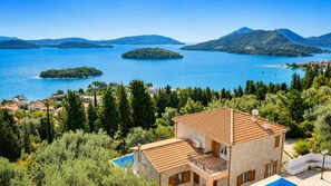 Une villa en pierre avec un toit en tuiles, une piscine et une vue sur un lac parsemé d’îles et bordé de montagnes.
