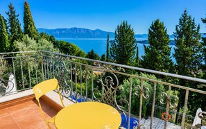 Ein Balkon mit gelbem Tisch und Stuhl, einem Metallgeländer und Blick auf einen See und Berge.