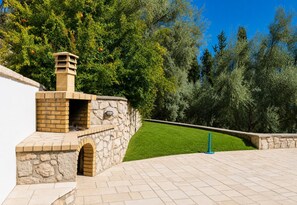 Ein aus Stein erbaueter Kamin im Freien mit einer Ziegelbogenkonstruktion, umgeben von einer gepflasterten Terrasse und einem gepflegten Rasen.
