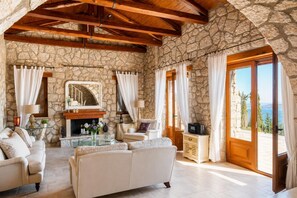 Ein Wohnzimmer mit Steinwänden, einem Kamin, Sofas und Meerblick durch eine große Tür.