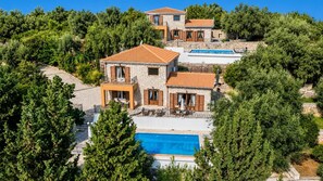 Un bâtiment en pierre à plusieurs étages, doté d’une piscine et entouré d’une végétation luxuriante.