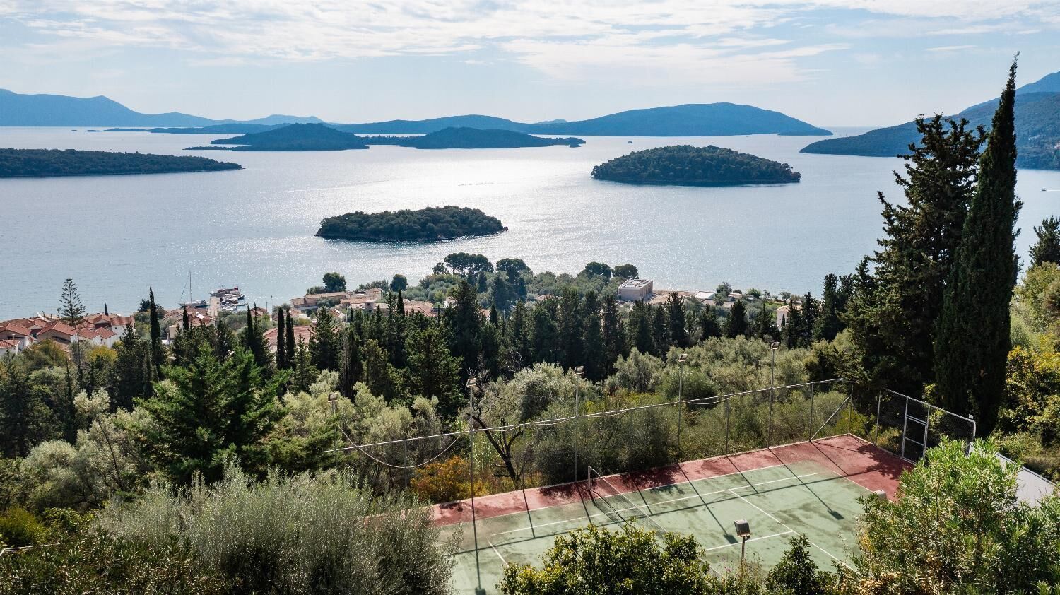 A tennis court surrounded by trees and overlooking a lake with multiple islands.