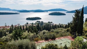Uma quadra de tênis rodeada por árvores e com vista para um lago com várias ilhas.
