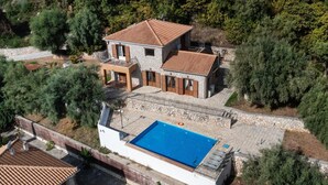 Uma casa de dois andares com piscina, rodeada por árvores.