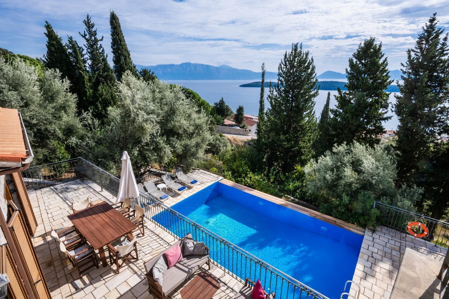 Schwimmbad mit Blick auf Berge und See, umgeben von Bäumen und Gartenmöbeln.