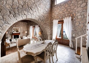 Una habitación de paredes de piedra con chimenea, una mesa de comedor y una escalera.