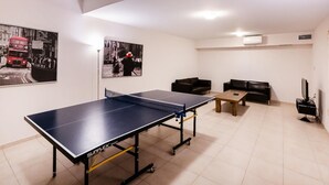 Um quarto com mesa de pingue-pongue, dois sofás, uma televisão e dois cartazes na parede.