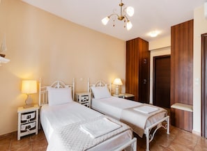 Habitación de hotel con dos camas individuales, mesitas de noche con lámparas, un armario de madera y un candelabro.
