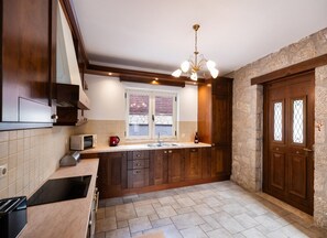 A kitchen with wooden cabinets, a built-in oven, a microwave, and a window with blinds. - Villa Galatia - Three Bedroom Villa, Sleeps 6 (Perigiali)