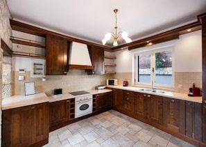 A modern kitchen with wooden cabinets, a built-in oven, a microwave, and a window with a view of the outdoors. - Villa Galatia - Three Bedroom Villa, Sleeps 6 (Perigiali)
