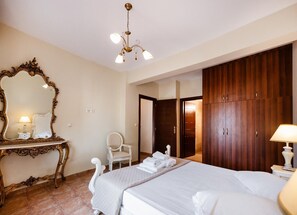 A hotel room with a bed, a mirror, a chair, a wardrobe, and a chandelier. - Villa Galatia - Three Bedroom Villa, Sleeps 6 (Perigiali)