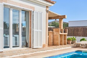 Área da piscina com um pátio, um espaço de estar coberto e vista para uma casa com portas de correr.