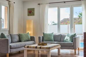 A living room with two grey sofas, a striped coffee table, and a large window with curtains. - Villa Casa Martin - Three Bedroom Villa, Sleeps 6 (Portocolom)