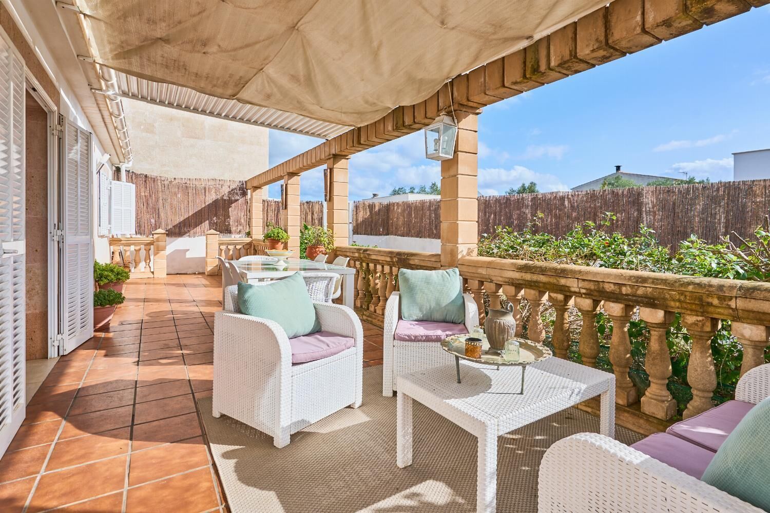 A covered patio with wicker furniture, a table, and potted plants.