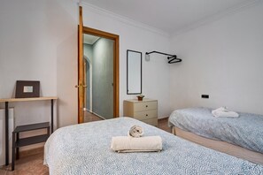 Quarto com duas camas, porta de madeira, penteadeira, espelho e luminária na parede.