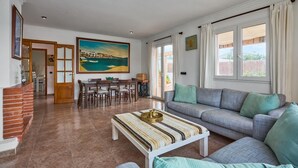 A spacious living area with a sofa, a dining table with chairs, a fireplace, and a large painting on the wall. - Villa Casa Martin - Three Bedroom Villa, Sleeps 6 (Portocolom)