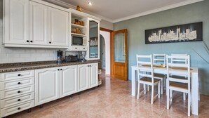 A kitchen with white cabinets, a granite countertop, and a dining area with white chairs and a table. - Villa Casa Martin - Three Bedroom Villa, Sleeps 6 (Portocolom)
