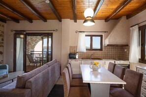Une cuisine chaleureuse avec un coin repas, des poutres en bois et une vue sur l’extérieur, visible à travers la porte.