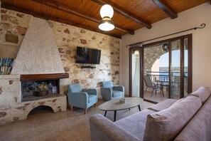 Een kamer met stenen muren, een open haard, een televisie, een bank en een balkon met uitzicht.