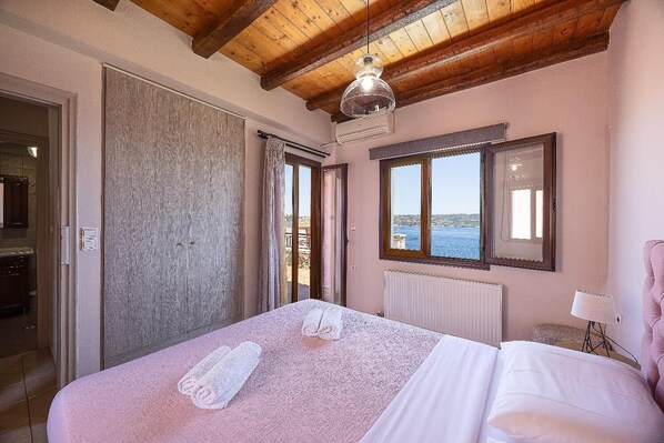 A bedroom with a large bed, a view of the sea, a wooden ceiling, and a window with a mirror. - Villa Forteza - Three Bedroom Villa, Sleeps 6 (Kalami)