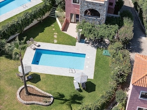 Vue aérienne d’un espace piscine comprenant une piscine rectangulaire, des chaises longues et un bâtiment en pierre doté d’une fenêtre.