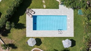 Eine Vogelperspektive auf einen rechteckigen Swimmingpool mit zwei Liegestühlen und zwei Sonnenschirmen auf einer gepflegten Rasenfläche.