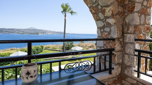 Ein Balkon mit Steinmauer, einer Palme und Blick auf das Meer und hügelige Ferne.