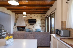 A cozy living area with a stone fireplace, a flat-screen TV mounted on the wall, and a kitchen area with a microwave. - Villa Forteza - Three Bedroom Villa, Sleeps 6 (Kalami)