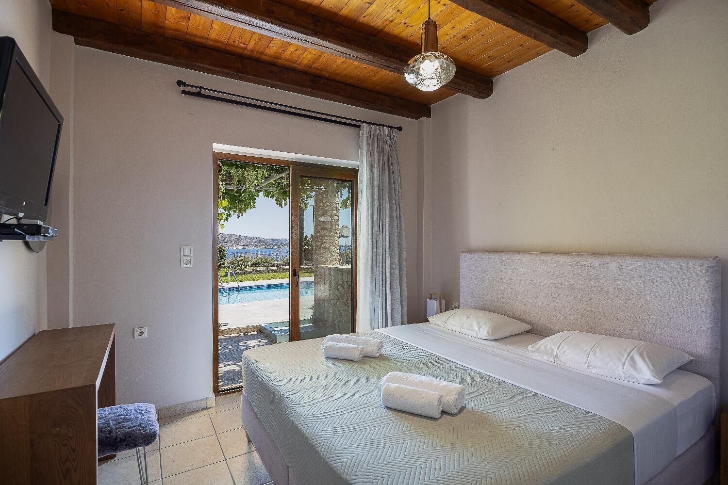 Ein Schlafzimmer mit Bett, Schreibtisch, Fernseher und Blick auf Pool und Grünflächen.