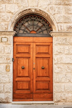 Una doppia porta in legno sormontata da un arco in metallo, incastonata in un muro di pietra.