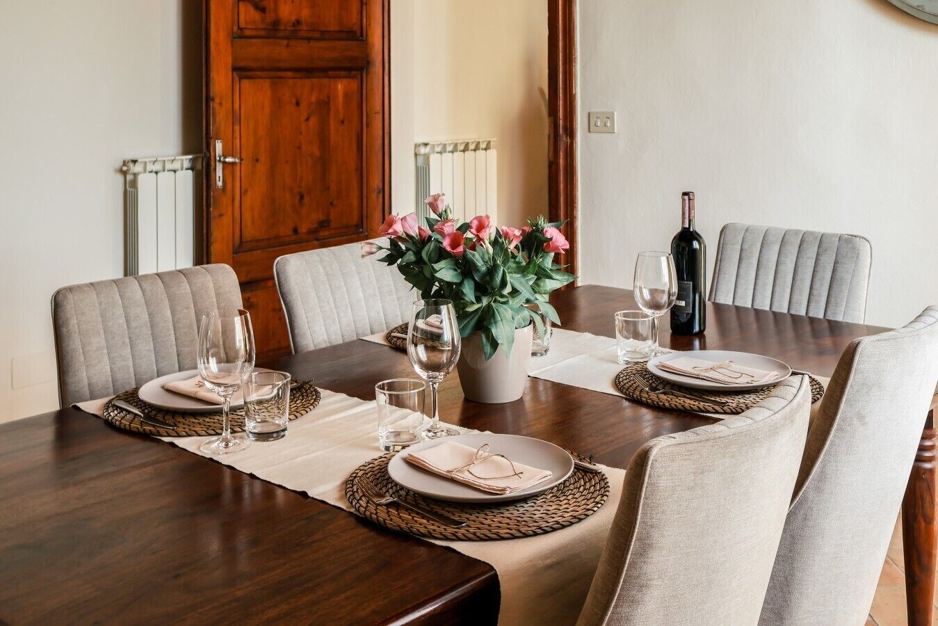 Une table à manger dressée pour quatre personnes, avec un vase de fleurs, une bouteille de vin et des verres.
